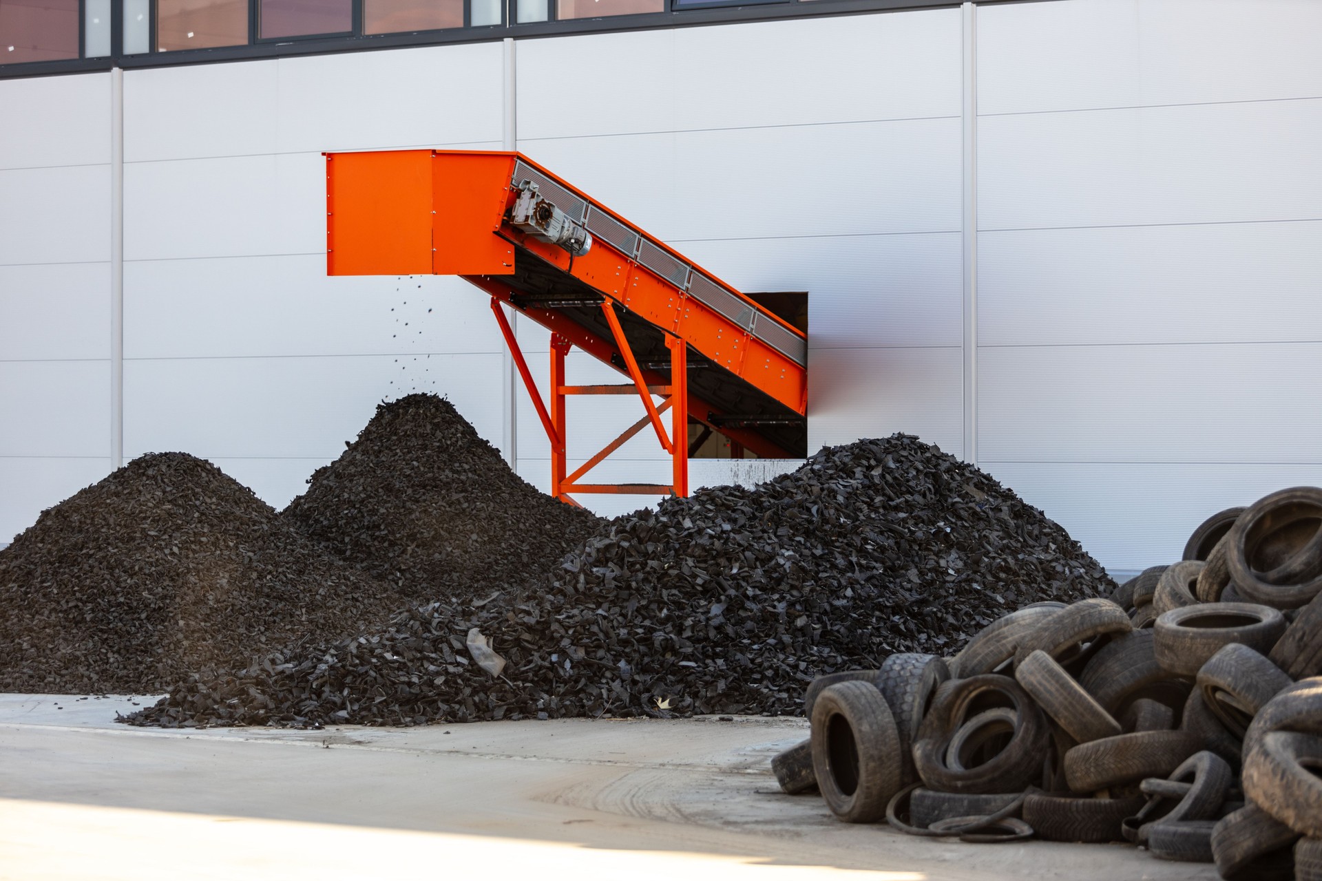 Tire recycling facility with shredded rubber piles and conveyor belt