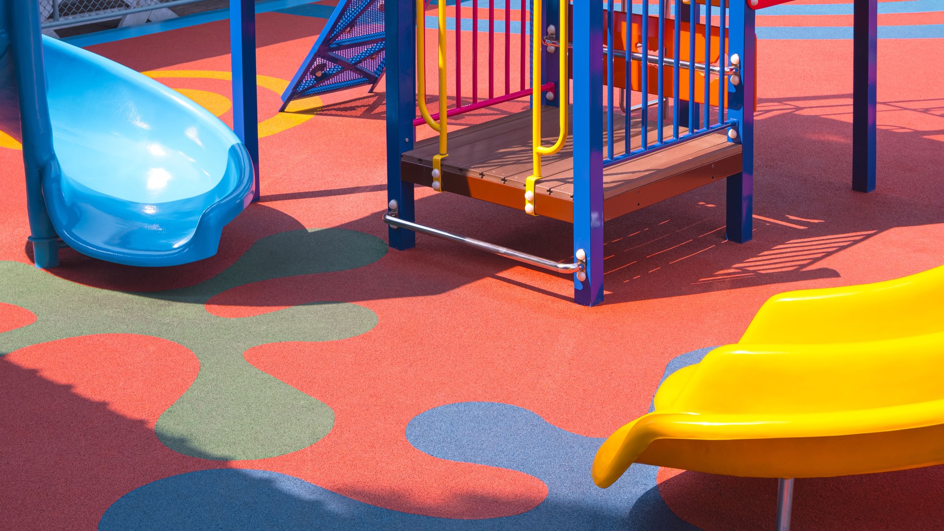Yellow and blue slides with playground climbing equipment on colorful rubber floor in outdoors playground area at kindergarten school